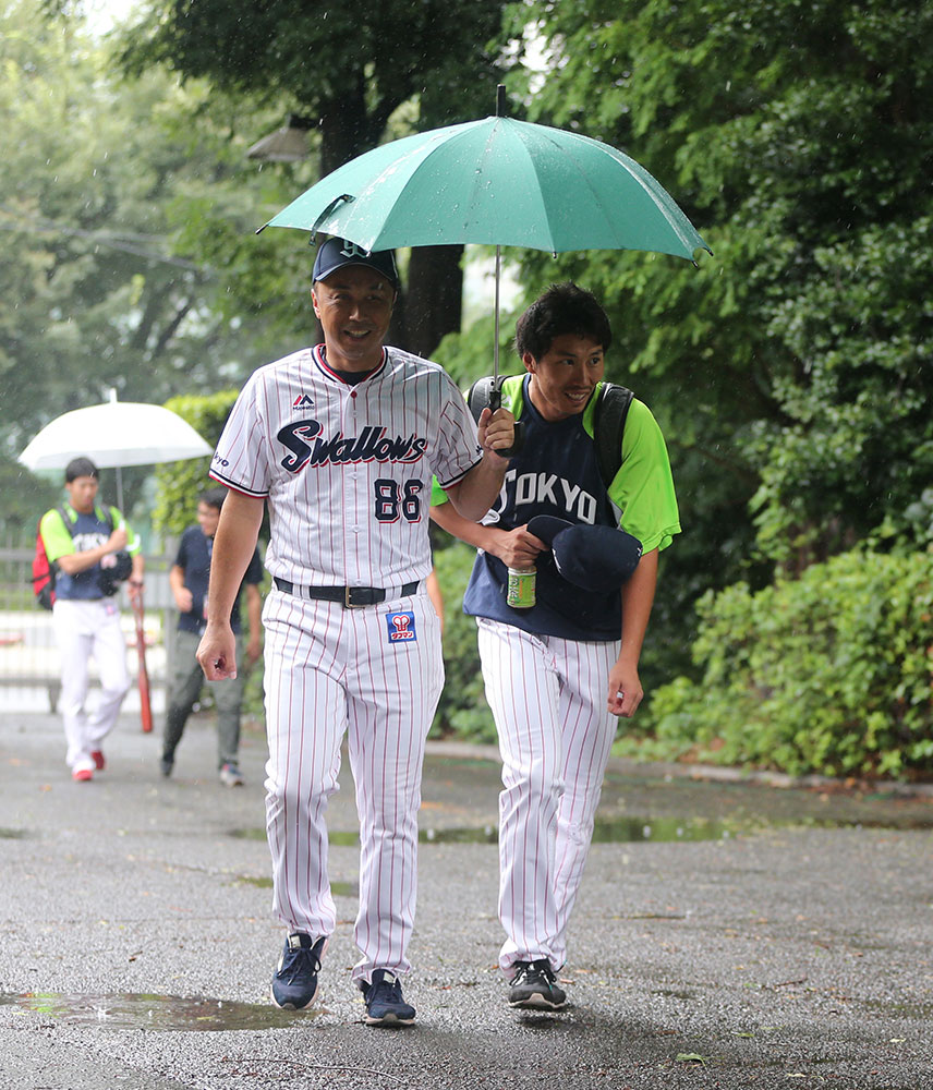 ８日、宮本ヘッドコーチに傘をさしてもらいながら室内練習場へ向かうヤクルト・上田