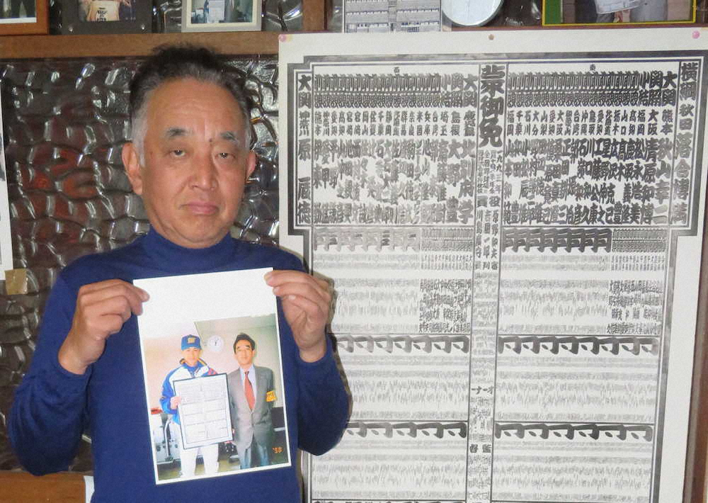 1998年、新大関に昇進した日本野球界番付を持つイチローと塩村和彦代表の写真を示す塩村氏、後ろは実寸の日本野球界番付