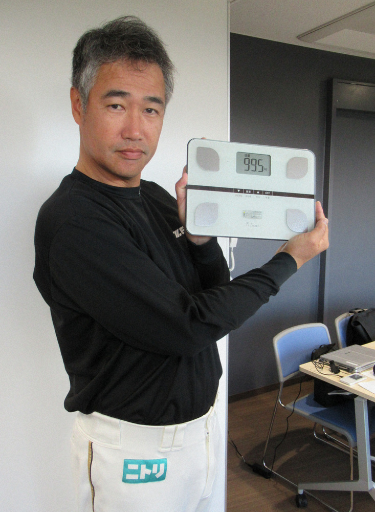 ９９.５㌔を示す体重計をしたり顔で掲げる日本ハム・木田コーチ
