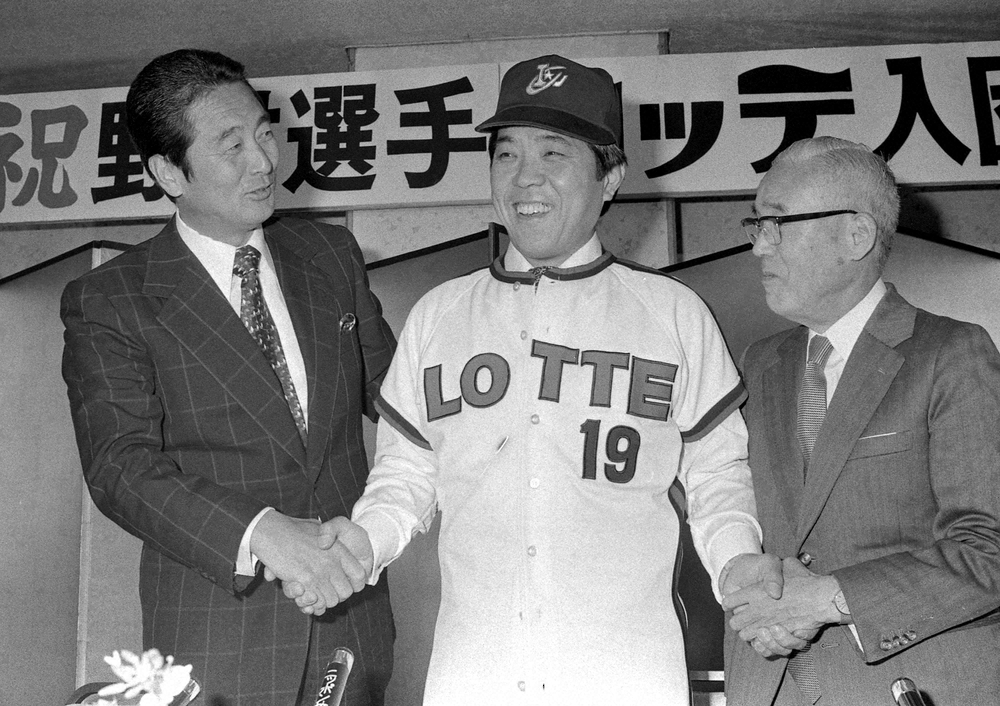 ロッテ入団発表会見で背番号19のユニホームに袖を通し金田正一監督（左）、松井静郎球団社長（右）と笑顔で握手する野村克也（1977年）