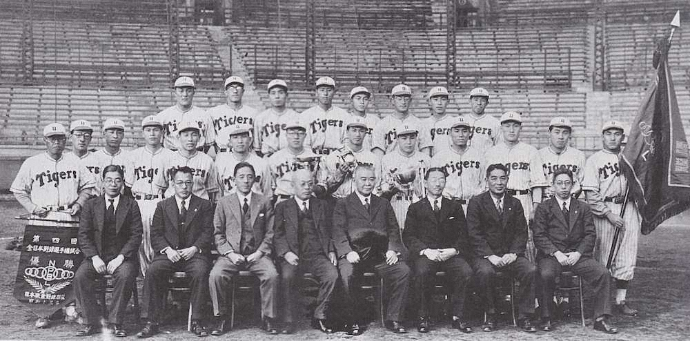 1938年、日本一となったタイガースのメンバー。左端が石本秀一監督。右端で優勝旗を持つのは藤村富美男＝阪神球団発行『阪神タイガース　昭和のあゆみ』より＝