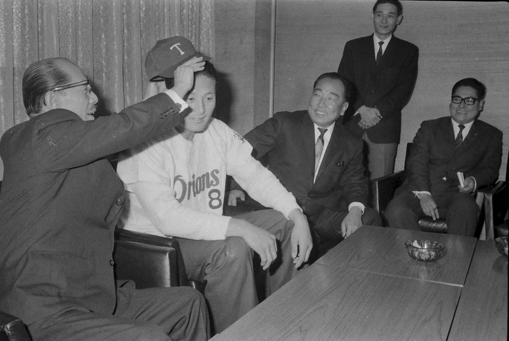 東京からドラフト1位で指名され、入団発表の席で永田オーナー（左）から帽子をかぶせてもらう近大の有藤内野手（同２人目）