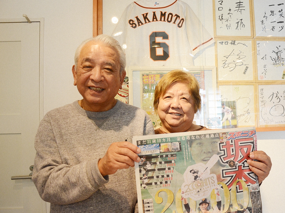 9日付の本紙を手に坂本の2000安打達成を喜ぶ芹川敏恵さん（右）と夫・寛行さん