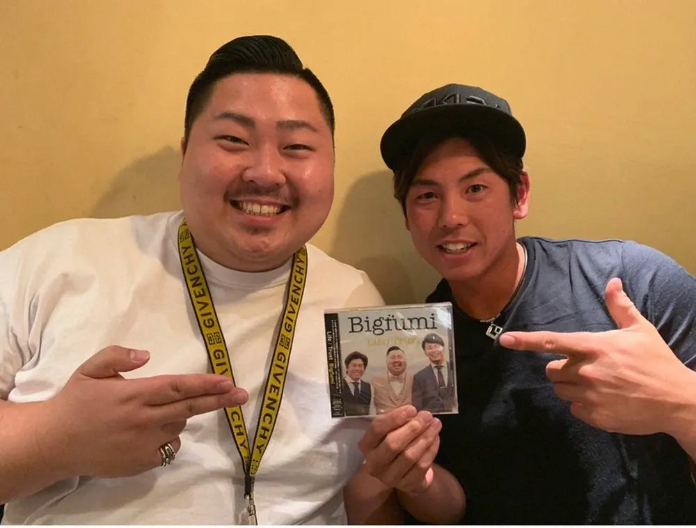 自身のCDを手にした福岡大先輩の梅野隆太郎捕手（右）とポーズを決めるシンガー・ソングライターのBigfumi