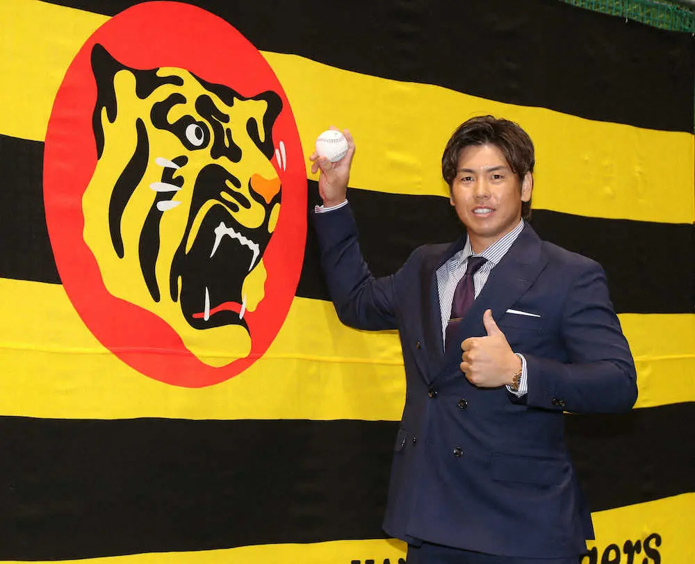 契約更改交渉を終えた阪神・梅野は球団旗を前にポーズをとる（撮影・大森　寛明）