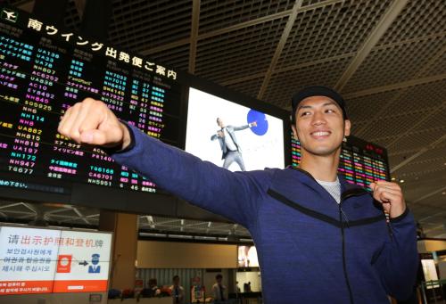 渡米前、成田空港の出発便案内に映し出されたボルトの広告を背にポーズを取る村田