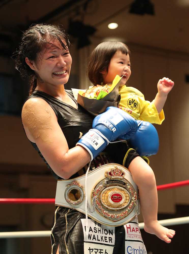 日本女子初代バンタム級王座についた吉田は愛娘の実衣菜ちゃんを抱いて笑顔を見せる