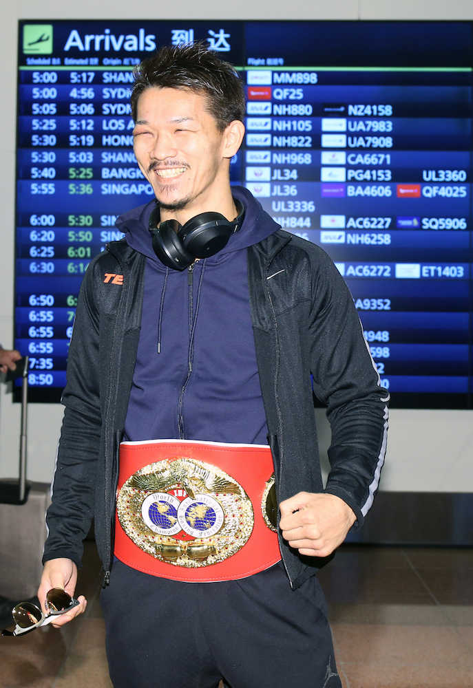 羽田空港に到着し、ベルトを巻きながら笑顔をみせるＩＢＦ世界スーパーフェザー級王者の尾川