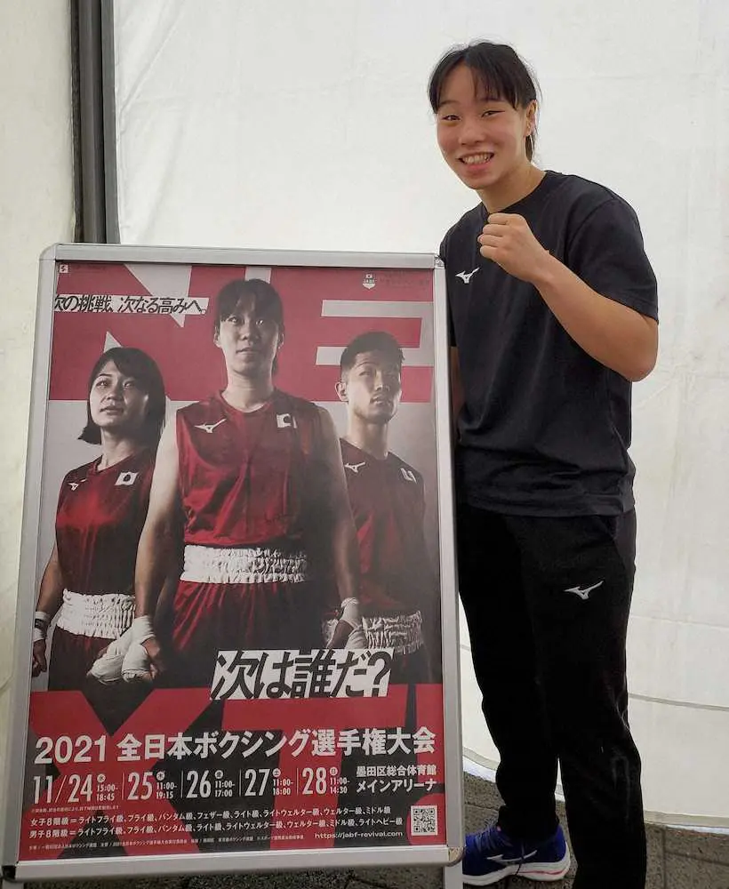 全日本選手権のポスターの横でポーズをとる入江