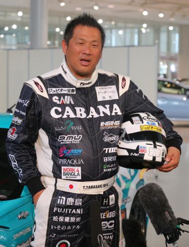 レーシングスーツで報道陣の質問に答える山崎氏