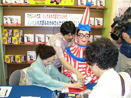 「くいだおれ」代表取締役会長の柿木道子さん（左）にサポートされサイン会を行ったくいだおれ太郎