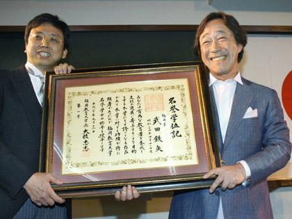 福岡教育大の大後忠志学長（左）から「名誉学位記」を笑顔で受けとる武田鉄矢