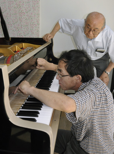 再生したピアノの調律を見守る井上晃雄さん（奥）