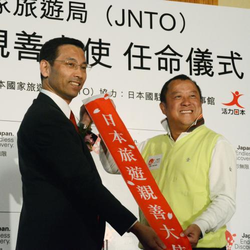 27日、香港のホテルで「日本旅行親善大使」に任命され、日本政府観光局香港事務所の平田真幸所長（左）からたすきを渡される俳優エリック・ツァン（共同）