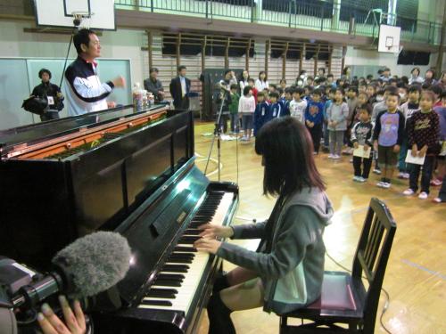 村沢茜里さんの伴奏で校歌を合唱する久之浜第一小の児童たち。被爆ピアノの後方が中畑氏