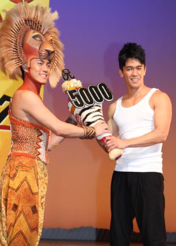 劇団四季「ライオンキング」通算５０００回達成祝いに駆けつけ、シンバ（左）に笑顔でシマウマの肉を贈呈する武井壮