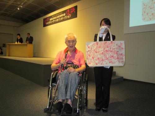 車椅子に乗り元気な姿を披露した永六輔。赤とんぼをあしらったバッグが30万円で落札され驚いた表情をみせた