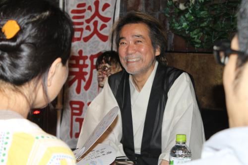 怪談俳句の会で笑顔を見せる稲川淳二。後方には不気味な人形が顔をのぞかせていた