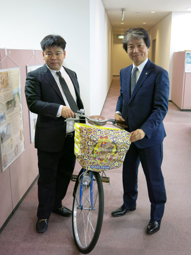 自らデザインした自転車用ひったくり防止カバーを紹介するジミー大西（左）と笑顔の田中誠太八尾市長