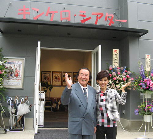 ０９年６月、完成した劇場前に立つ愛川さんと妻うつみ宮土理
