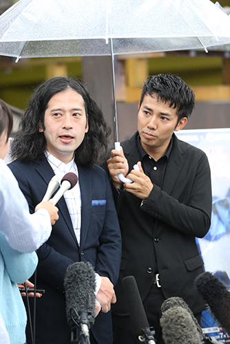 今月１６日、芥川賞を受賞し、報道陣の質問に答える又吉直樹の隣で傘を持つ相方の綾部祐二