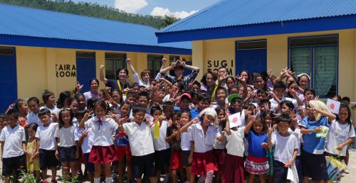 建築されたフィリピン・ドゥラグ町のダカイ小学校の校舎をバックに、生徒たちと喜びを表現するｗ－ｉｎｄｓ．の（後方左２人目から）千葉涼平、橘慶太、緒方龍一。緒方の右後方は平哲夫社長