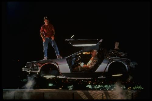 バック・トゥ・ザ・フューチャー２に登場するデロリアン。ボンネットの上に乗っているのが主人公マーティ（マイケル・Ｊ・フォックス）、運転手はドク（クリストファー・ロイド）（Ｃ）１９８９　Ｕｎｉｖｅｒｓａｌ　Ｓｔｕｄｉｏｓ　ａｎｄ　Ｕ－Ｄｒｉｖｅ　Ｐｒｏｄｕｃｔｉｏｎｓ’Ｉｎｃ．　Ａｌｌ　Ｒｉｇｈｔｓ　Ｒｅｓｅｒｖｅｄ．