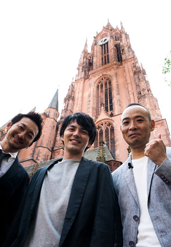 ドイツ・フランクフルトの大聖堂を背に笑顔の（左から）波岡一喜、林遣都、久万真路監督