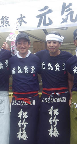 「熊本元気食堂」の看板を前に肩を組む（左から）神田正輝と舘ひろし