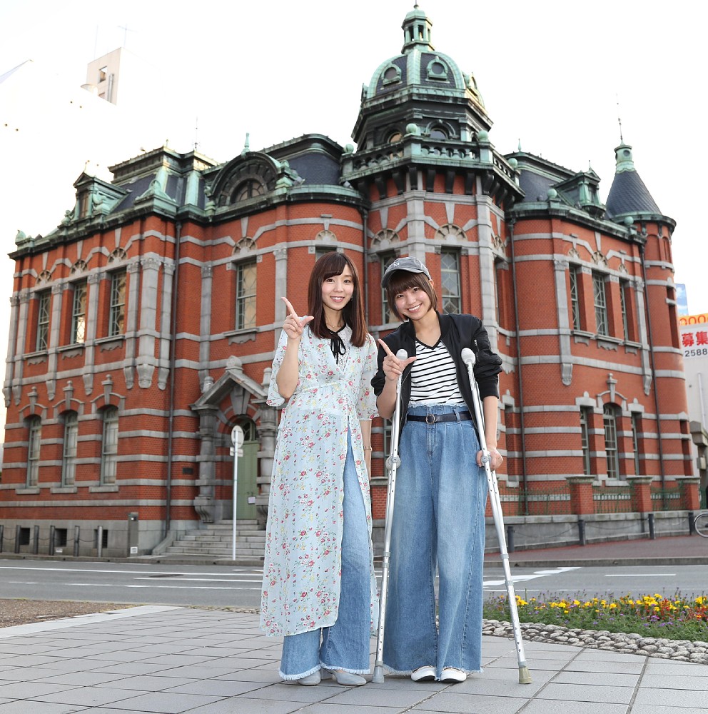 松葉杖姿の天野なつ（右）と吉川千愛は福岡市赤煉瓦文化館を背にポーズする