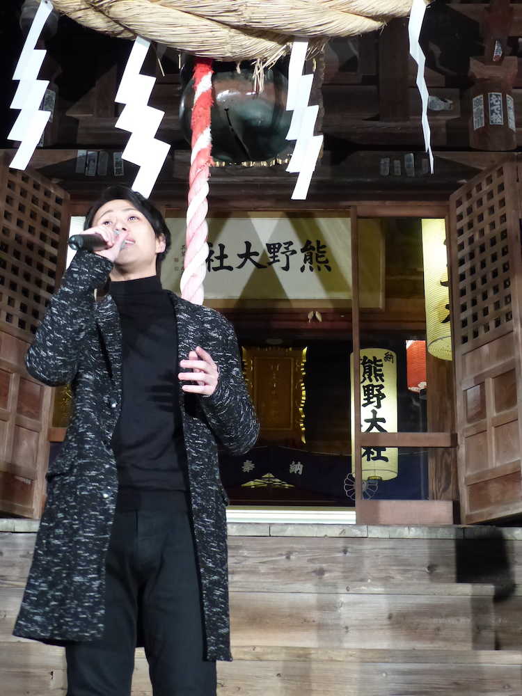 熊野大社の境内をバックに笑顔を浮かべて「上を向いて歩こう」を歌う林部智史