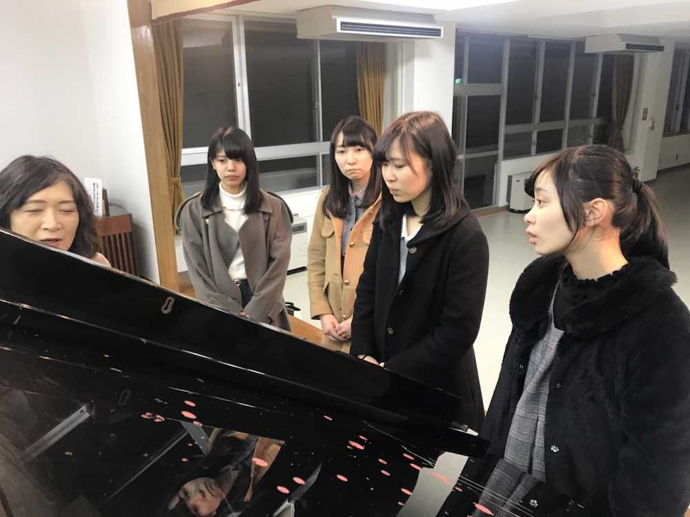宮城県七ヶ浜町で、被災後に修理したピアノを前に所有者の女性（左）から説明を受けるコウベリーズの（右から）大出姫花、黒谷真琴、森島みなみ、岡野春香