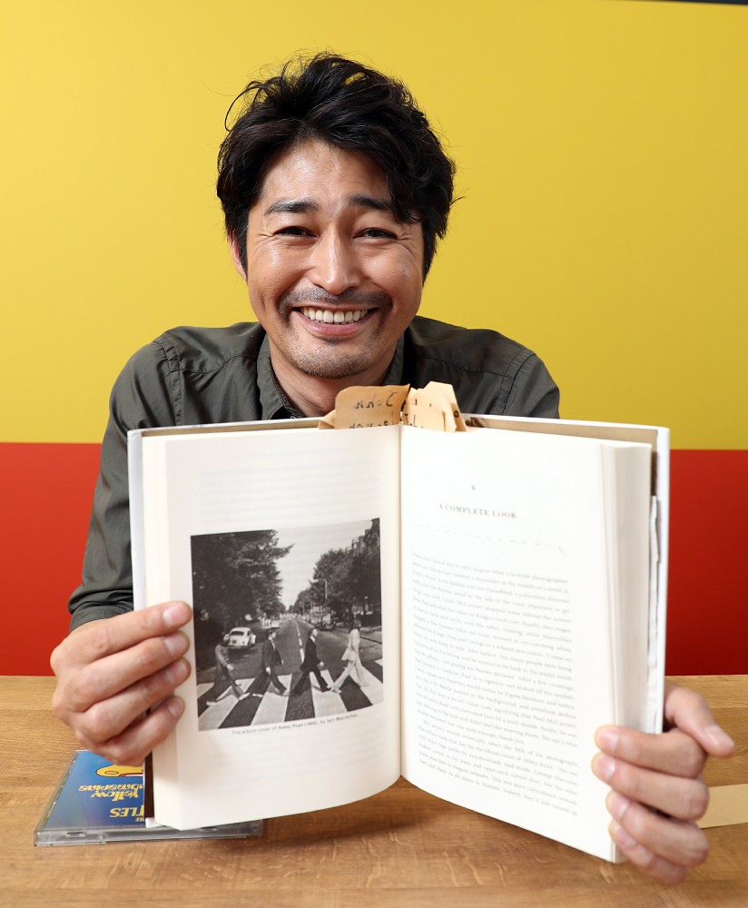 ビートルズの衣装を長年仕立てた故トミー・ナッタ―さんの本を持って笑顔の安田顕