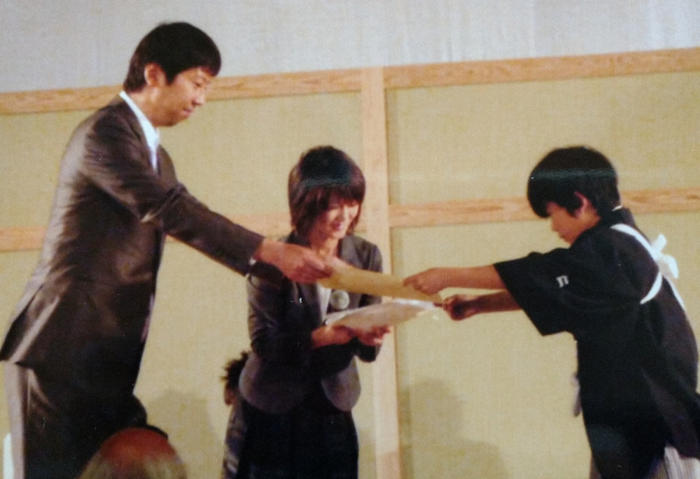 11年、将棋大会で優勝し後に師匠となる杉本八段から賞状を受け取る少年時代の藤井七段