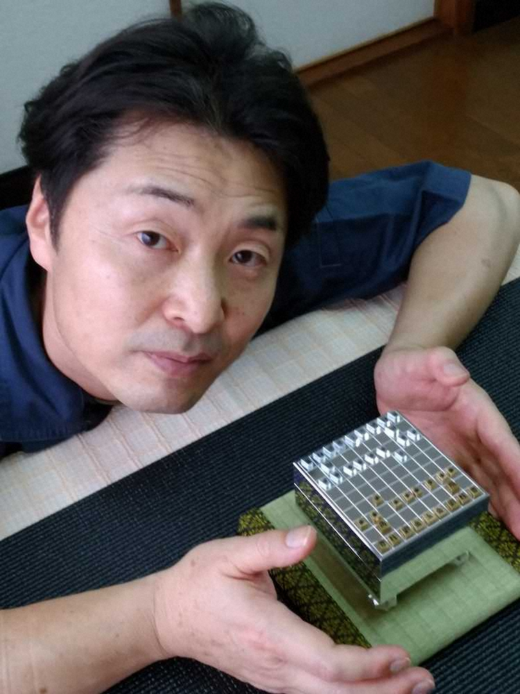 ジュラルミン製のミニチュア将棋セットを手にする伏屋勝彦社長
