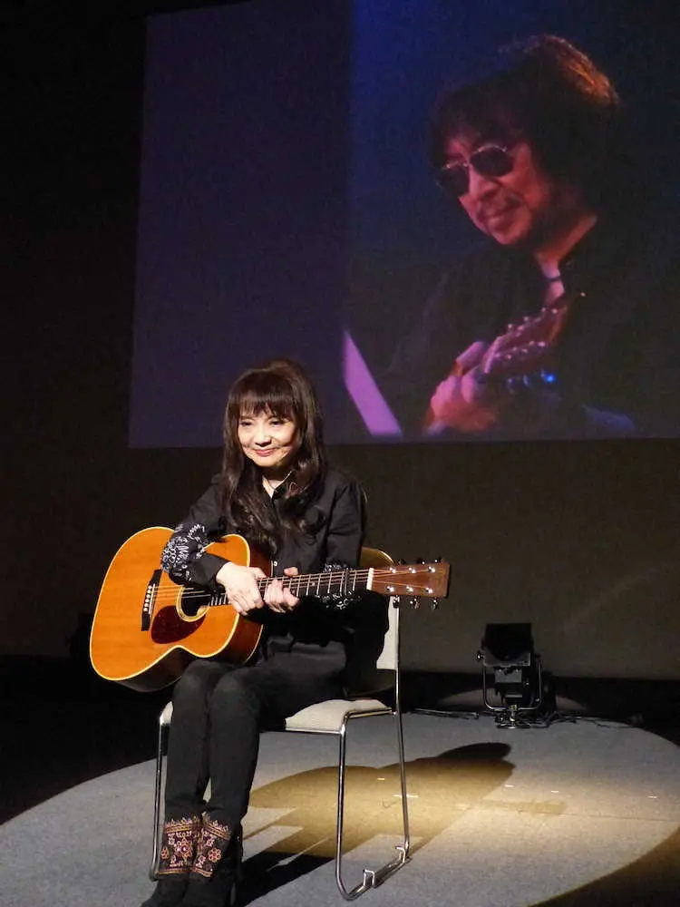 昨年7月に亡くなった夫でギタリストの安田裕美さんの写真をバックにギターを抱える山崎ハコ