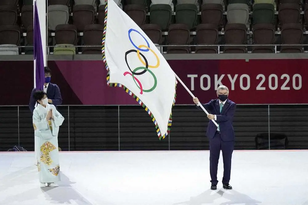 東京都の小池百合子知事（左）から受け取った五輪旗を振るIOCのバッハ会長（共同）