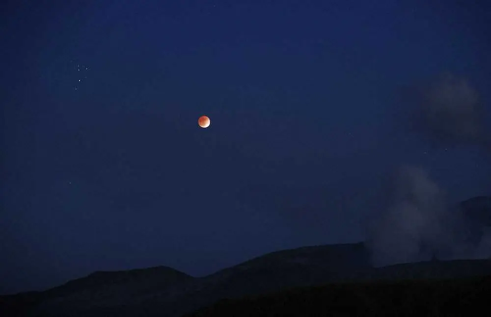19日午後5時58分、白煙を上げる阿蘇山の中岳（右下）と部分月食。左上はプレアデス星団（すばる）