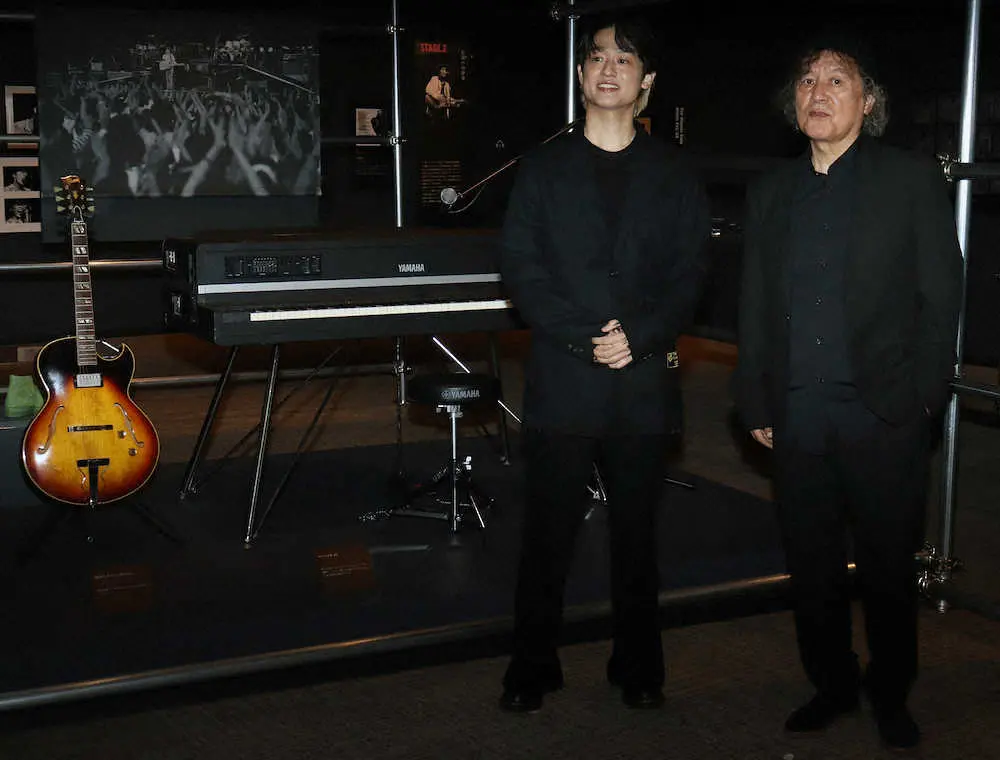 尾崎豊さんが愛用したピアノやギターの前で笑顔を見せる尾崎裕哉（左）と須藤晃プロデューサー