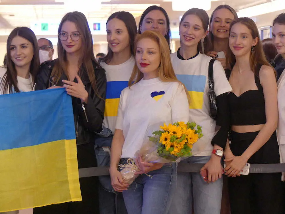 ウクライナのモデルたちが空港ロビーで出迎える中、花束を持って記念撮影するチーナ・カーロリ