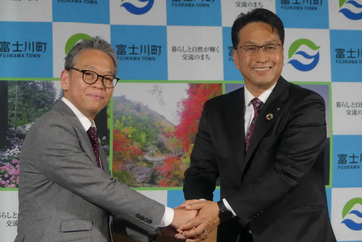 【画像・写真】オフィシャルパートナー協定を締結し握手する菅井敦社長（左）と望月利樹町長