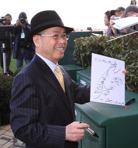 定年で引退する池江郎調教師はレース前、ファンに書いたサイン色紙を手に笑顔を見せる