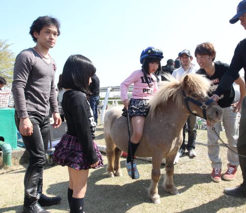 関東騎手クラブ主催の花見会でポニーの背でポーズをとる女の子。左は江田照男騎手、右は後藤浩輝騎手