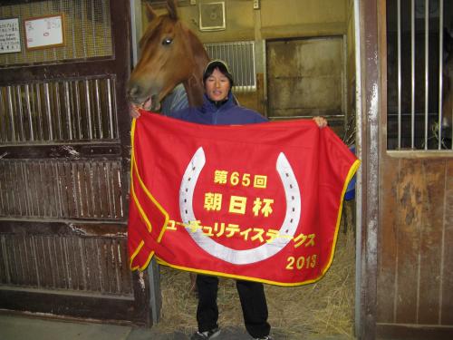 朝日杯ＦＳを３戦無敗で制したアジアエクスプレスと優勝記念の馬服を誇らしげに披露する田中良太助手