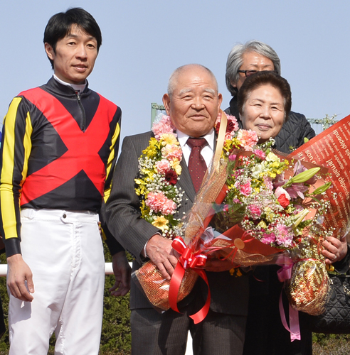 花束を贈られ多くの関係者と記念写真を撮る松田博師