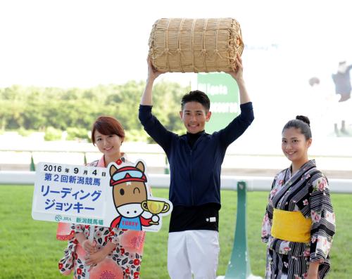 新潟競馬リーディングジョッキーに輝いた戸崎圭太騎手は俵を掲げポーズをとる。左は今井美穂、右は山田彩乃