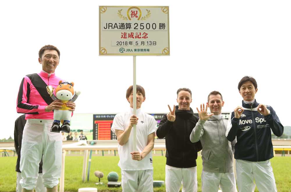 東京４ＲジェイケイマッチョでＪＲＡ通算２５００勝達成の蛯名（左）は（右から）武豊、Ｍ・デムーロ、ルメールから「２５００」の手文字で祝福される。看板を持つのは松岡
