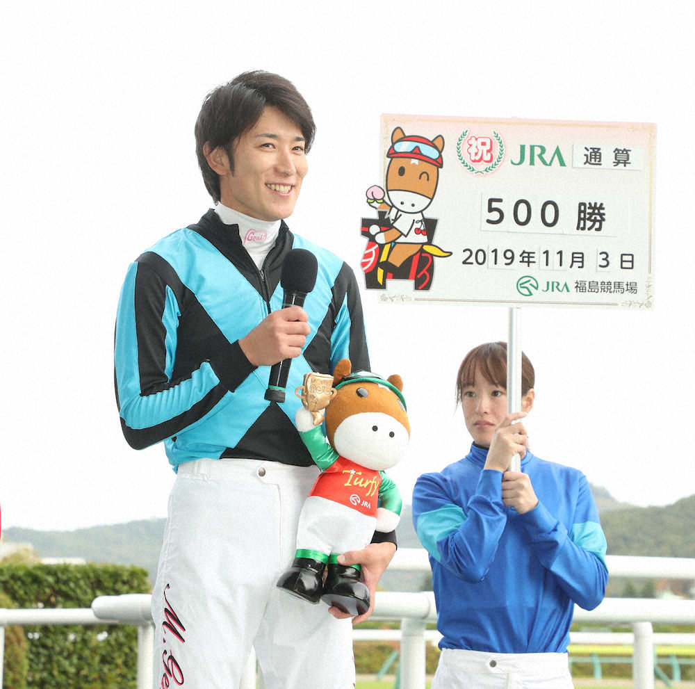 11月3日の福島9Rで丸山元気（左）は通算500勝達成の看板を妹弟子・藤田菜七子に持ってもらい笑顔を見せる