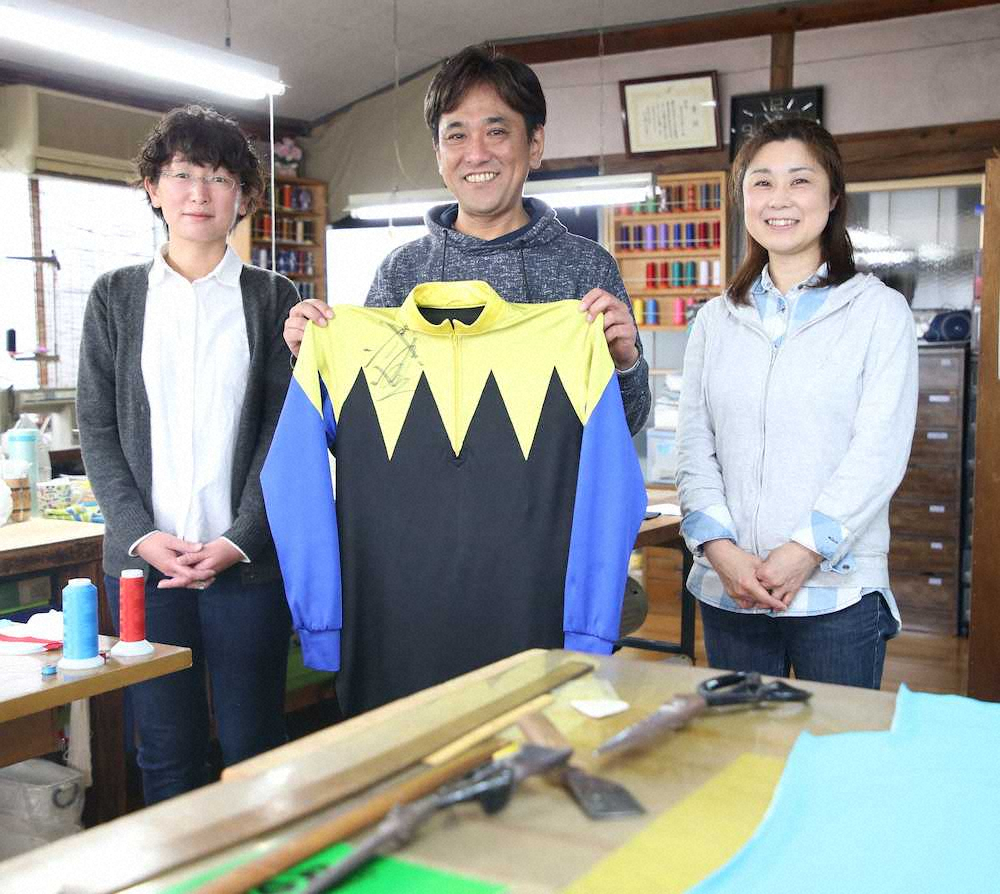 武豊のサイン入りの勝負服を手に笑顔を見せる「河野テーラー」の河野社長（中央）と岡田由美子さん（左）、河野祐子さん