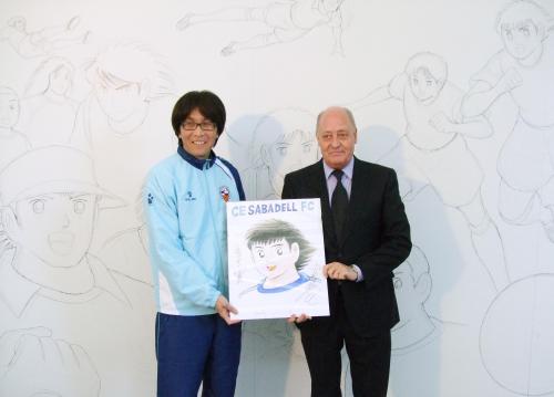 「キャプテン翼」のデッサン画が描かれたキャンバスの前に立つ作者の高橋陽一氏（左）とスペイン２部リーグ、サバデルの関係者